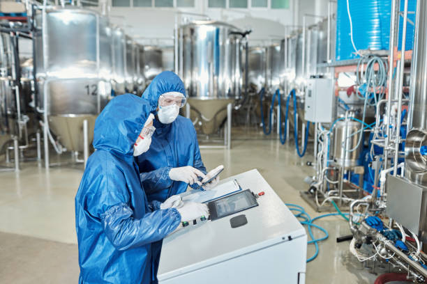 Pharmaceutical engineers in cleanroom suits monitoring biotech equipment for drug production using high-performance plastic systems